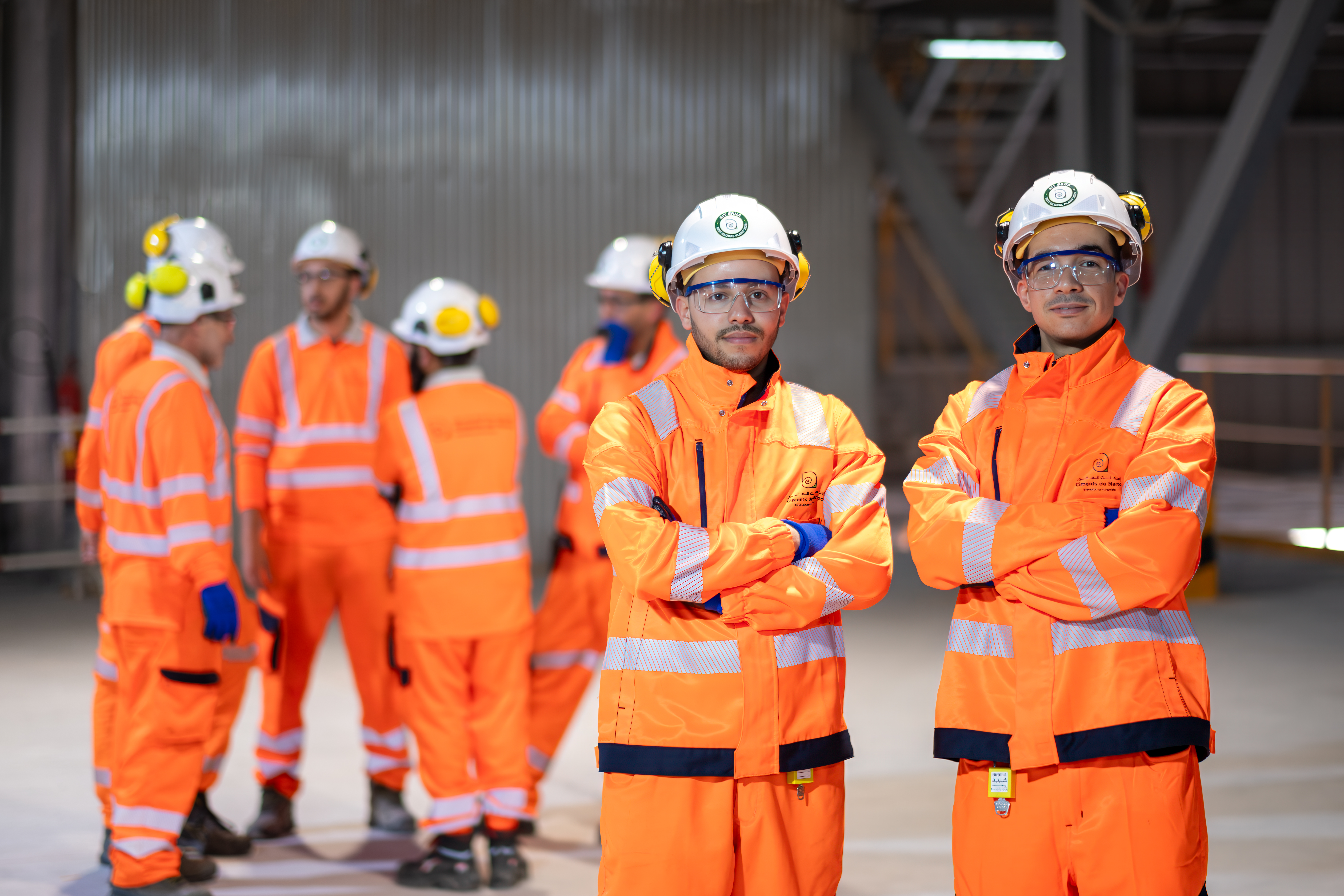 Des travailleurs en tenue de sécurité orange et casques se tiennent dans un site industriel moderne